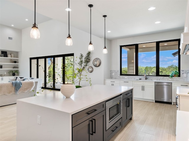 kitchen with stainless steel appliances, white cabinetry, sink, and pendant lighting