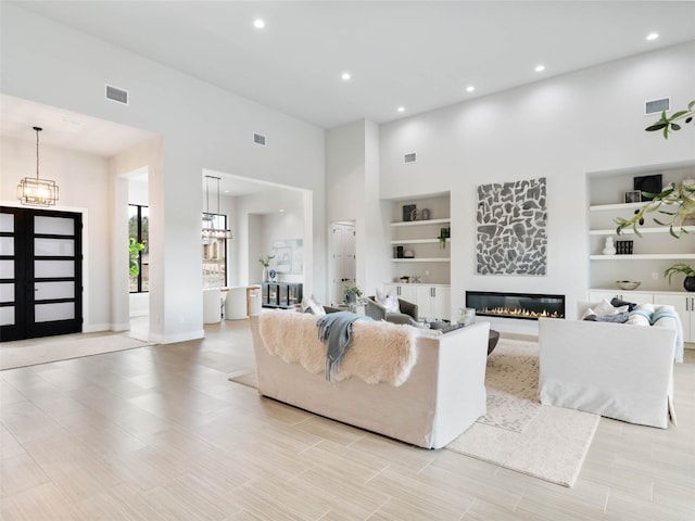 living room with a high ceiling, built in features, an inviting chandelier, and french doors