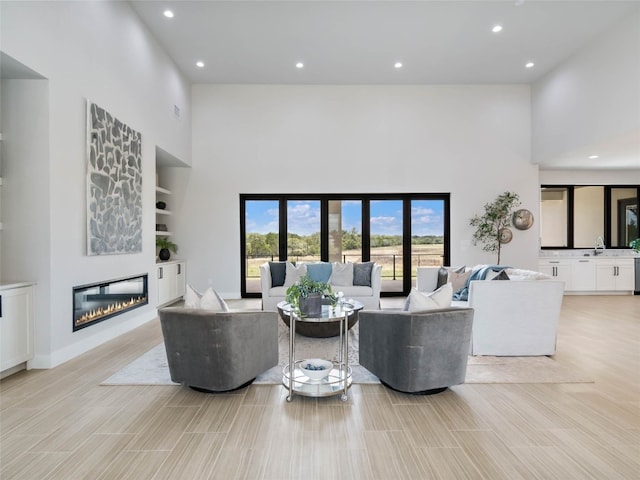 living room with a high ceiling, sink, light hardwood / wood-style flooring, and built in shelves