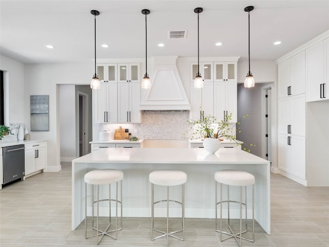 kitchen featuring a breakfast bar area, stainless steel dishwasher, custom range hood, a large island, and white cabinets