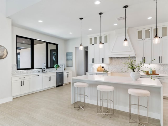 kitchen featuring dishwasher, premium range hood, a kitchen bar, white cabinets, and a kitchen island