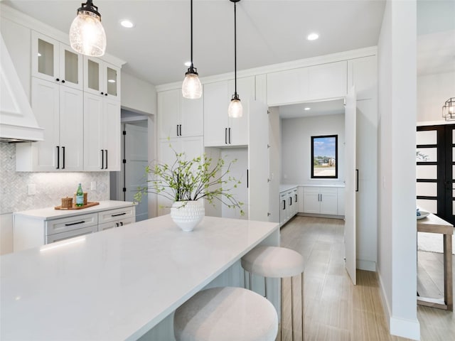 kitchen with premium range hood, a kitchen bar, white cabinetry, pendant lighting, and backsplash