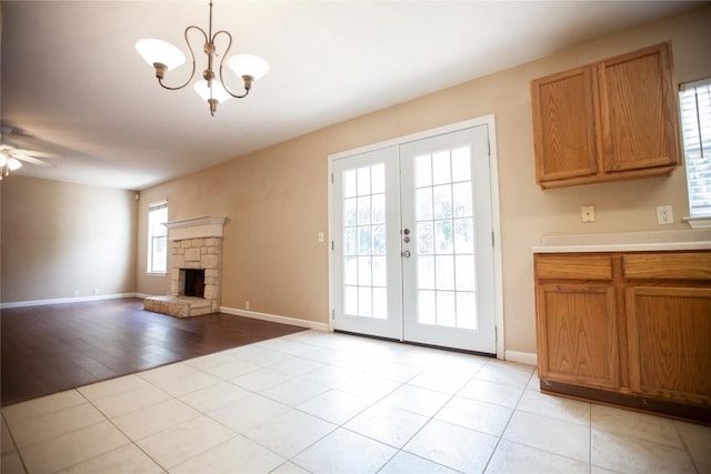 unfurnished living room featuring ceiling fan with notable chandelier, light tile patterned floors, a fireplace, and french doors