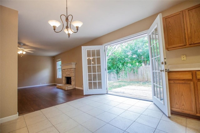 interior space with ceiling fan with notable chandelier, a stone fireplace, light tile patterned floors, and french doors