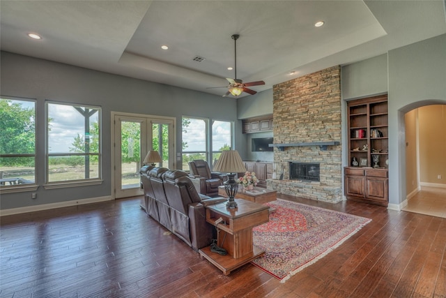 living room featuring ceiling fan, a fireplace, dark hardwood / wood-style floors, a raised ceiling, and built in features