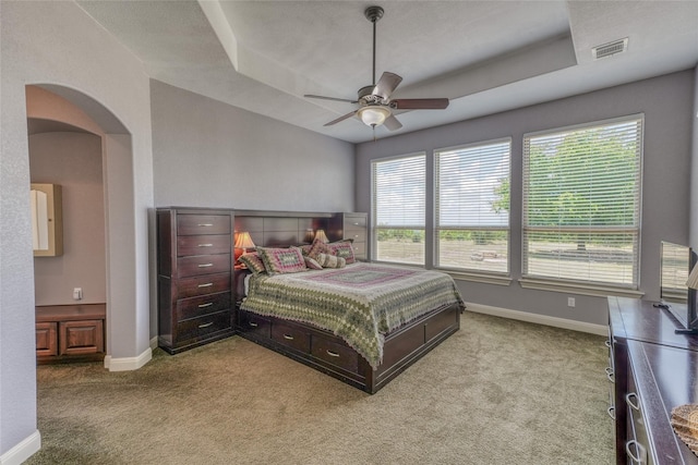 bedroom with ceiling fan, light colored carpet, and a raised ceiling