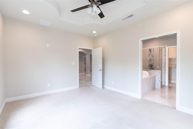 unfurnished bedroom with ensuite bath, a spacious closet, a raised ceiling, a closet, and ceiling fan