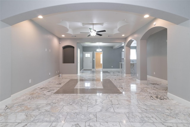 spare room featuring ceiling fan with notable chandelier and a tray ceiling