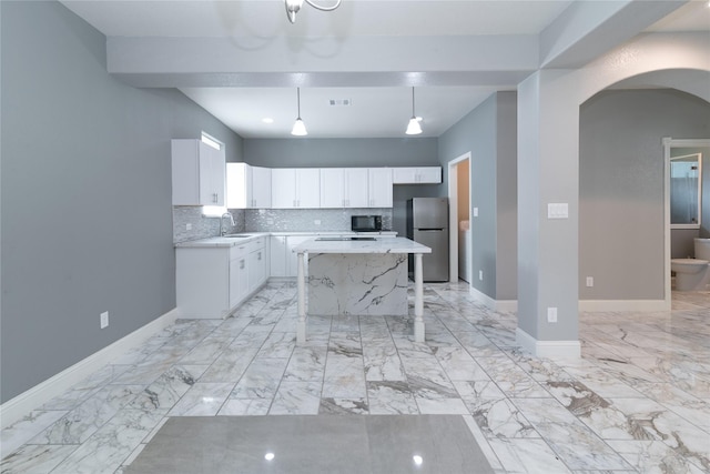 kitchen with white cabinetry, decorative light fixtures, stainless steel refrigerator, a kitchen island, and backsplash