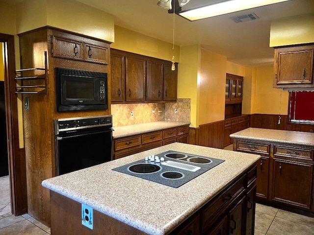 kitchen featuring black appliances, backsplash, light tile patterned floors, dark brown cabinetry, and a kitchen island