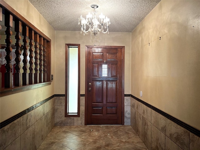 tiled foyer entrance featuring a notable chandelier, a textured ceiling, and tile walls