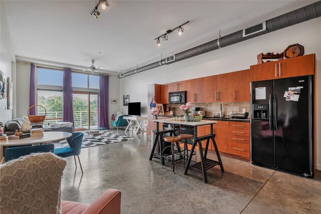 kitchen featuring black appliances, concrete flooring, a kitchen breakfast bar, ceiling fan, and decorative backsplash