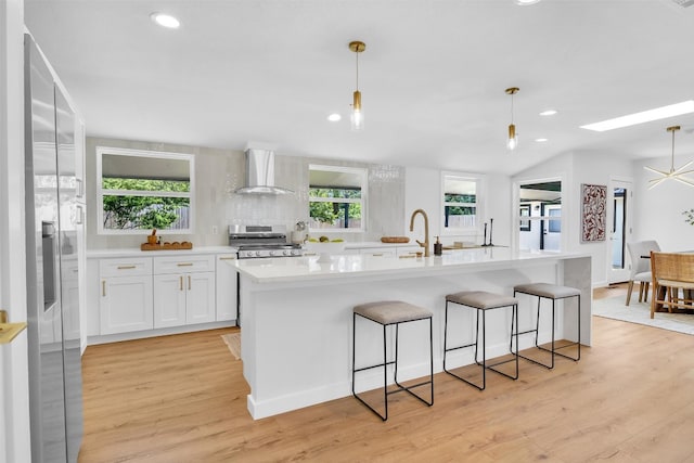 kitchen featuring hanging light fixtures, stainless steel stove, wall chimney exhaust hood, light hardwood / wood-style floors, and white cabinetry