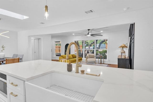 kitchen featuring a skylight, ceiling fan, sink, pendant lighting, and white cabinetry