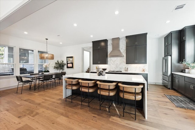 kitchen with hanging light fixtures, wall chimney exhaust hood, light hardwood / wood-style floors, and a kitchen island