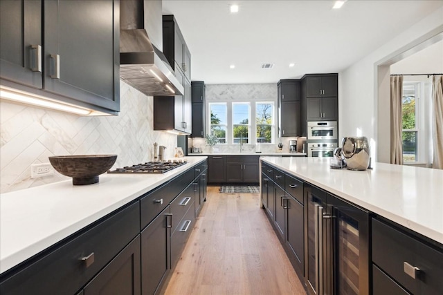 kitchen with wall chimney range hood, sink, appliances with stainless steel finishes, backsplash, and wine cooler