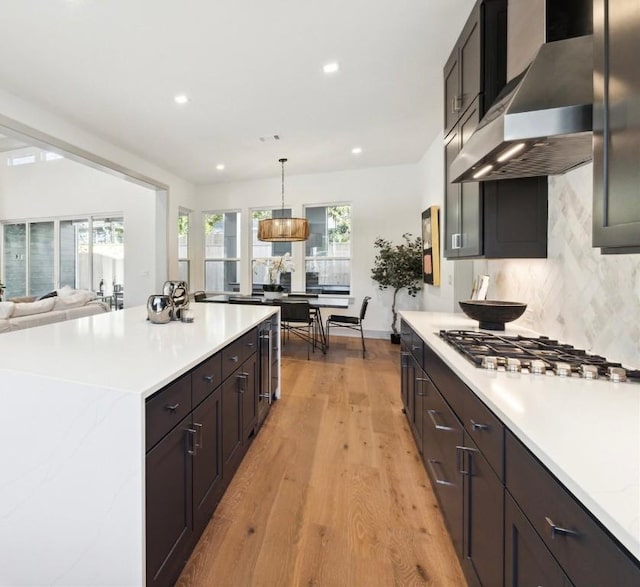 kitchen with wall chimney range hood, light hardwood / wood-style floors, decorative backsplash, decorative light fixtures, and stainless steel gas stovetop