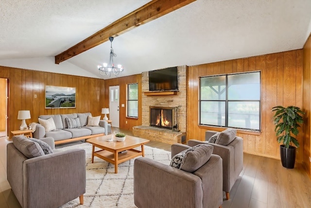 living room featuring wood walls, vaulted ceiling with beams, light wood-type flooring, a fireplace, and a notable chandelier