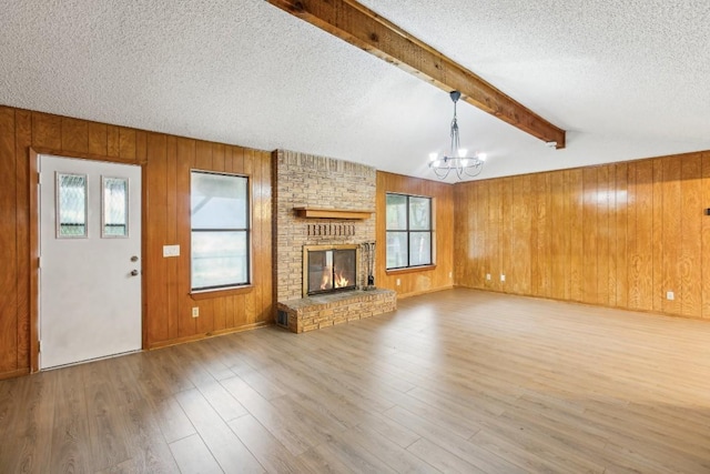 unfurnished living room featuring a fireplace, wood-type flooring, beamed ceiling, and a healthy amount of sunlight