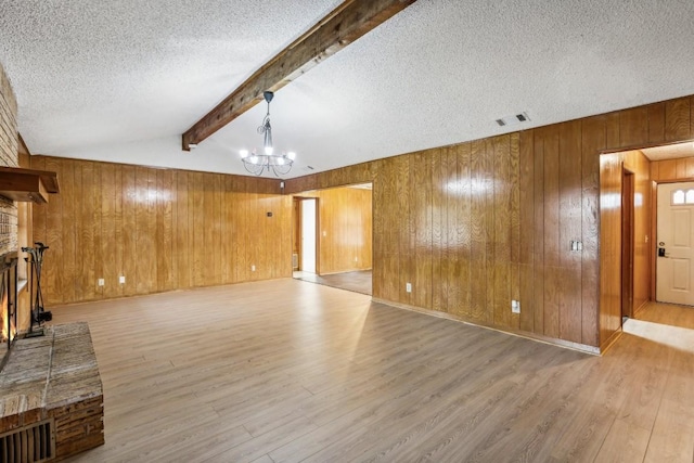 unfurnished living room featuring an inviting chandelier, wooden walls, a brick fireplace, vaulted ceiling with beams, and light hardwood / wood-style floors