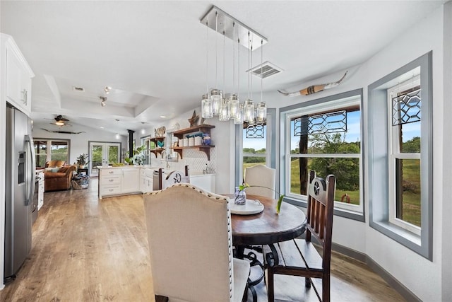 dining area with a raised ceiling, ceiling fan with notable chandelier, and light wood-type flooring