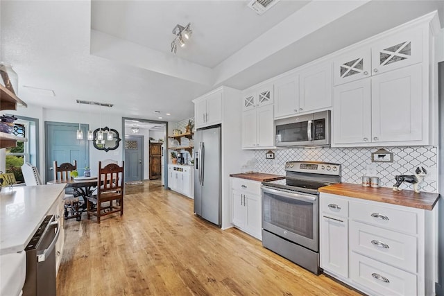 kitchen with decorative backsplash, stainless steel appliances, pendant lighting, white cabinets, and butcher block counters