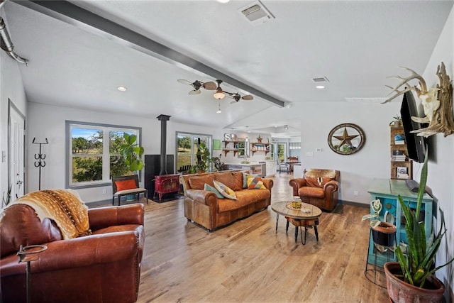 living room with vaulted ceiling with beams, light hardwood / wood-style floors, a wood stove, and ceiling fan