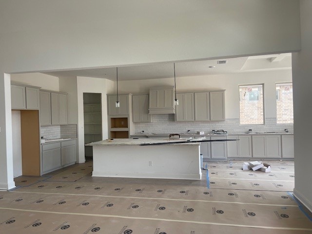 kitchen featuring backsplash, hanging light fixtures, a center island, light stone counters, and gray cabinets