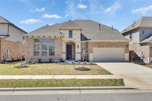 french country inspired facade featuring concrete driveway, a front yard, a shingled roof, a garage, and brick siding