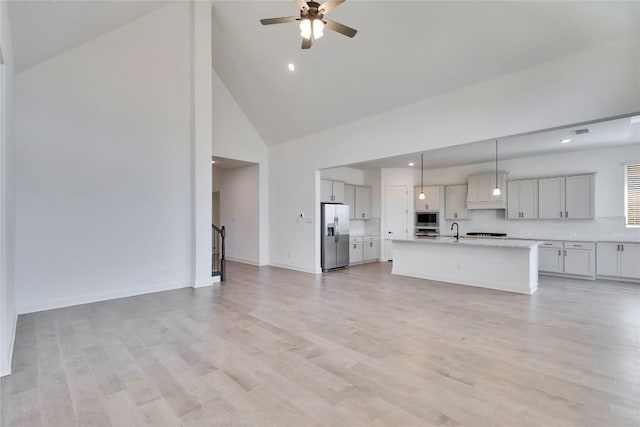 unfurnished living room featuring high vaulted ceiling, light wood-style flooring, a sink, baseboards, and ceiling fan