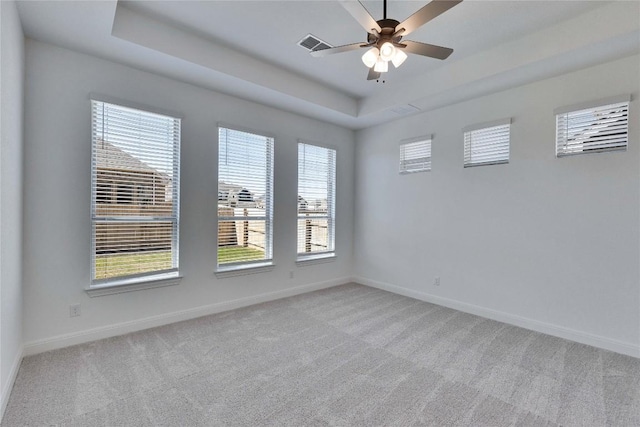 empty room with baseboards, a tray ceiling, light carpet, and visible vents