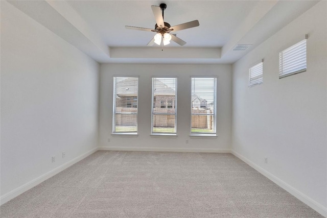 spare room featuring a tray ceiling, a ceiling fan, baseboards, and light carpet