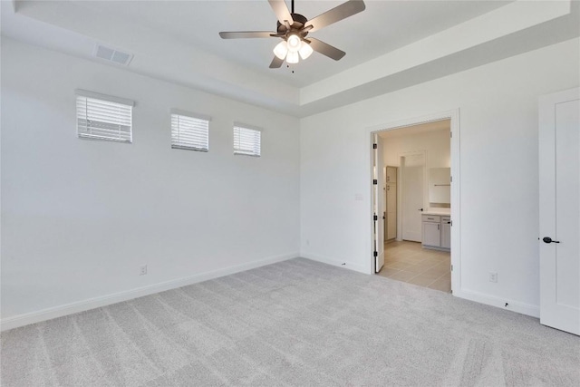 unfurnished bedroom with a tray ceiling, visible vents, light carpet, and baseboards