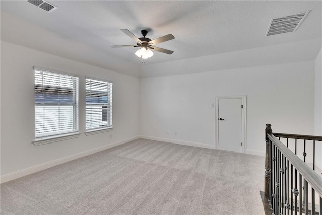 empty room featuring a ceiling fan, light colored carpet, visible vents, and baseboards