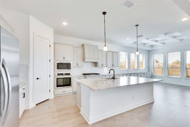 kitchen featuring visible vents, custom range hood, coffered ceiling, stainless steel appliances, and a sink