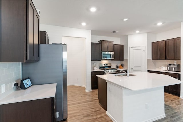 kitchen featuring light wood-type flooring, sink, stainless steel appliances, and an island with sink