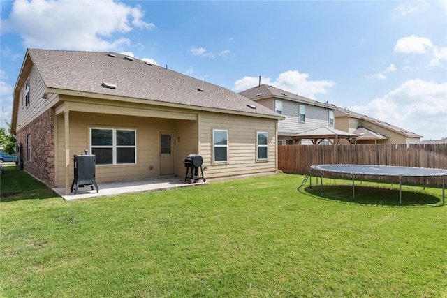 rear view of property featuring a trampoline, a patio area, and a lawn