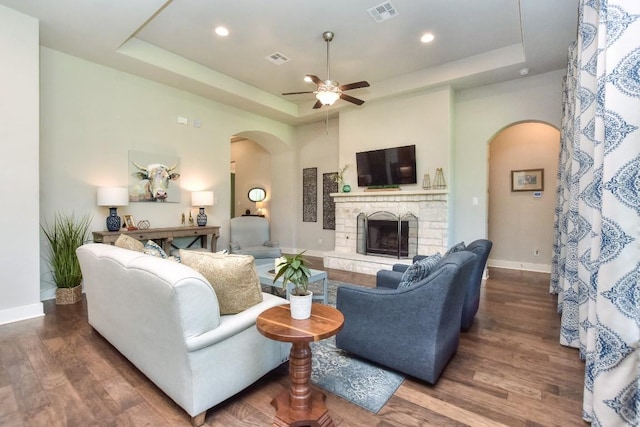 living room with ceiling fan, dark hardwood / wood-style floors, a raised ceiling, and a fireplace