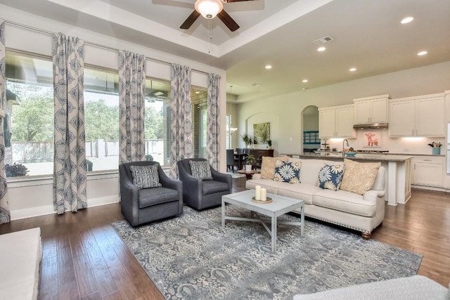 living room with ceiling fan, dark wood-type flooring, and a tray ceiling