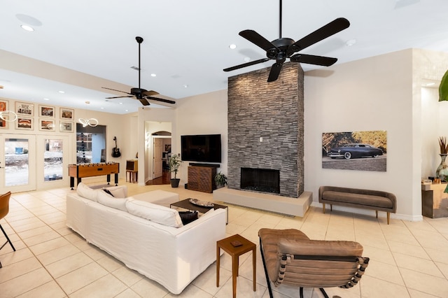 living room featuring a stone fireplace, light tile patterned floors, and ceiling fan