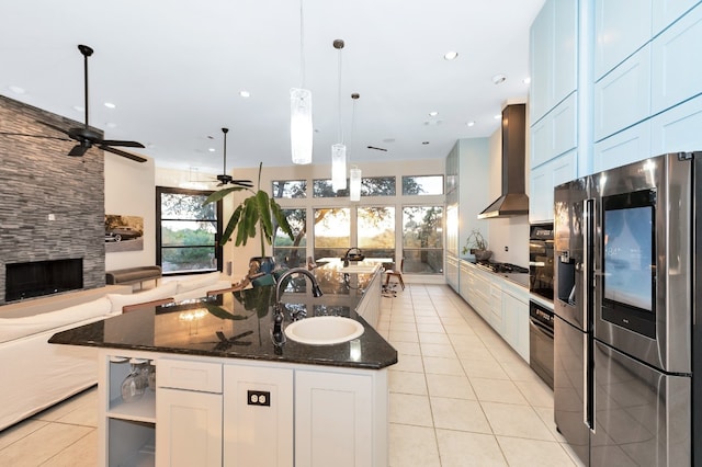 kitchen with appliances with stainless steel finishes, wall chimney range hood, sink, dark stone countertops, and ceiling fan