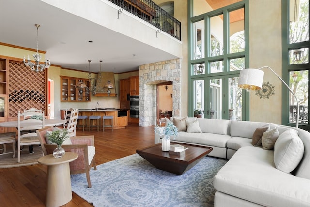 living room with a notable chandelier, hardwood / wood-style flooring, a high ceiling, crown molding, and sink