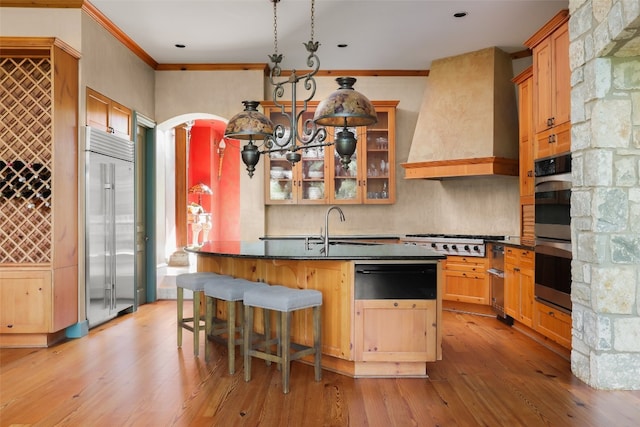 kitchen featuring premium range hood, light hardwood / wood-style flooring, appliances with stainless steel finishes, and a center island with sink