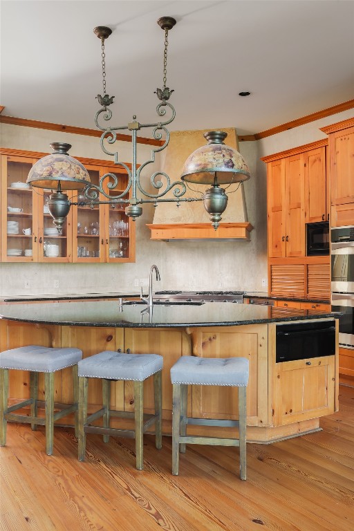 kitchen with black microwave, light hardwood / wood-style floors, a kitchen island, ornamental molding, and double oven