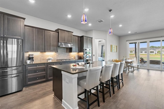 kitchen featuring a kitchen bar, stainless steel appliances, pendant lighting, wood-type flooring, and a center island with sink