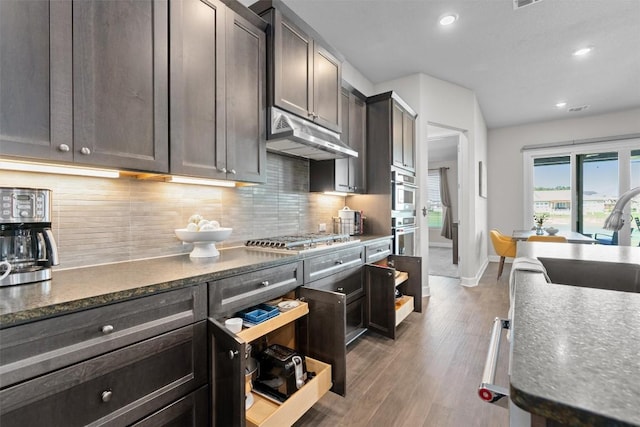 kitchen featuring sink, tasteful backsplash, dark hardwood / wood-style flooring, dark brown cabinets, and appliances with stainless steel finishes