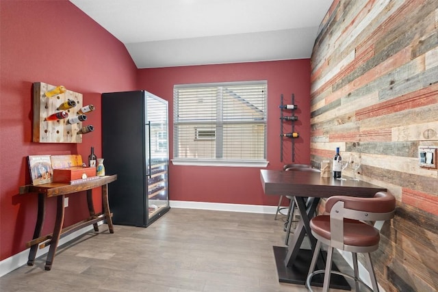 office area featuring wood-type flooring, lofted ceiling, wooden walls, and indoor bar