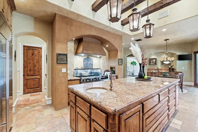 kitchen featuring sink, light stone counters, custom exhaust hood, a center island with sink, and pendant lighting