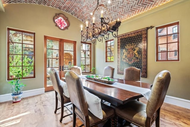 dining room with vaulted ceiling, light wood-type flooring, french doors, brick ceiling, and an inviting chandelier