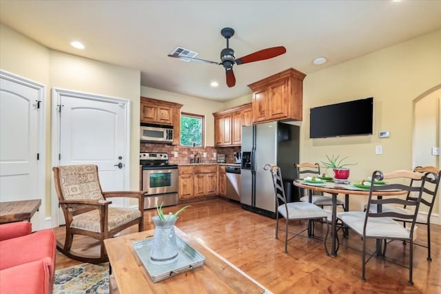 kitchen with stainless steel appliances, wood-type flooring, ceiling fan, and backsplash